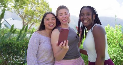 African american and diverse friends taking selfie with red smartphone in sunny garden