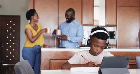 African American parents chatting with coffee while child studying on tablet in kitchen