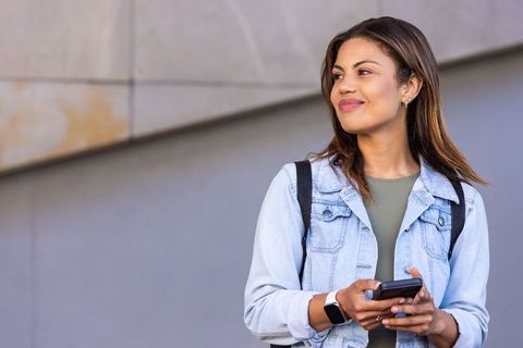 Young african american woman smiling and using smartphone outdoors in denim jacket