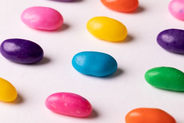 Vibrant close-up of an assortment of colorful jelly beans scattered on a white background. Perfect for themes of indulgence, sweet treats, children's parties, candy shops, or any content related to desserts and confectionery.
