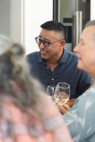 Mature friends gathering in kitchen laughing and holding wine glasses during relaxed dinner
