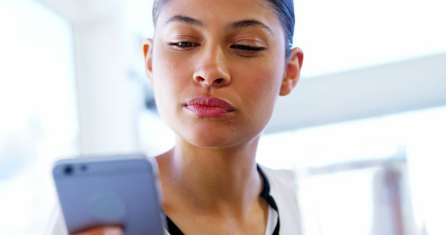 Woman gazing at smartphone with a serious expression indoors, showing technology dependency and focused searching or browsing. Ideal for illustrating modern communication, determination, and focus in advertisements, technology blogs, and educational content.