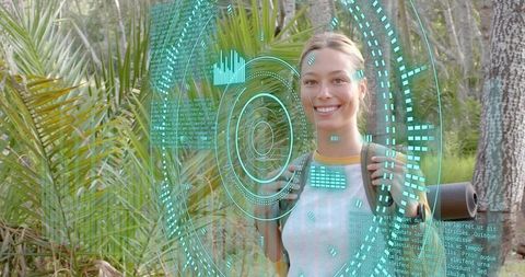 Smiling hiker with backpack and rolled mat using futuristic cyan HUD on forest trail