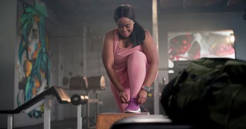 African american woman tying shoelace in pink activewear at urban gym with mural