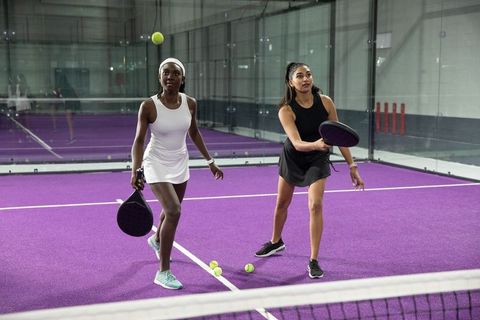 Women playing padel on vibrant purple court wearing athletic dresses