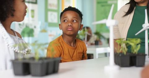 African american boy studying stem with seedlings and wind turbine model in classroom