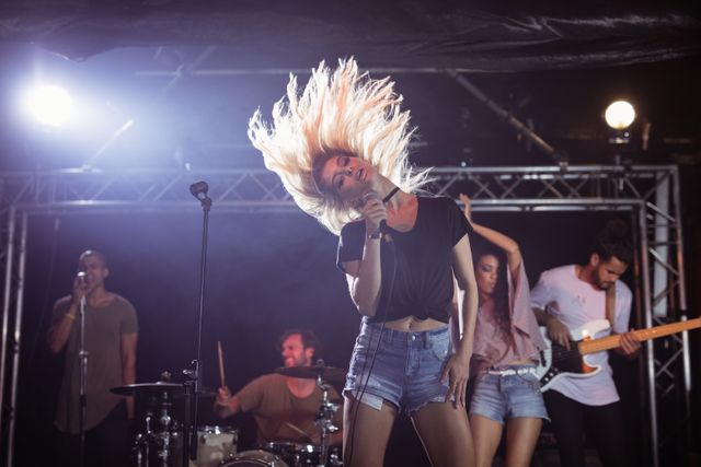 This image captures an energetic female singer performing with her band on stage during a music festival at a nightclub. The vibrant atmosphere, dynamic lighting, and enthusiastic expressions make it perfect for promoting live music events, concerts, nightlife venues, and entertainment-related content.