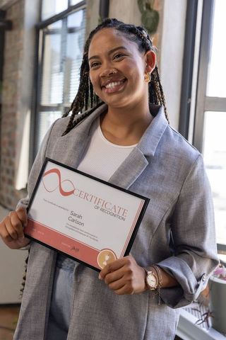 Confident woman holding certificate of recognition in modern office