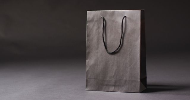 Black gift bag with black handles on dark grey background with copy space. Luxury treat, present, shopping, black friday sale and retail concept digitally generated image.