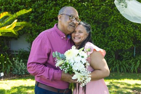 Senior african american couple embracing in sunlit garden holding bouquet of white flowers