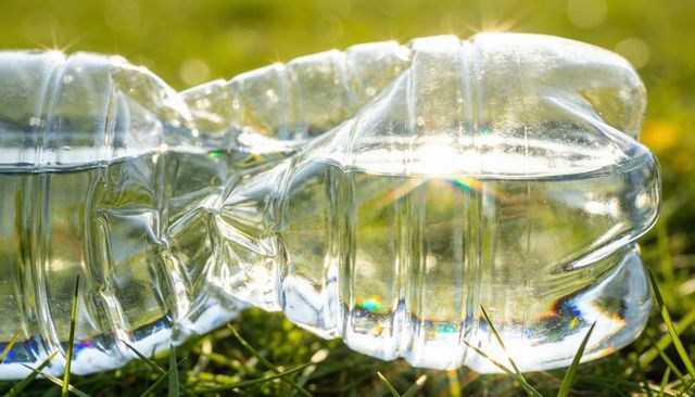 Crushed plastic water bottle reflecting sunlight on grass with prismatic sparkle