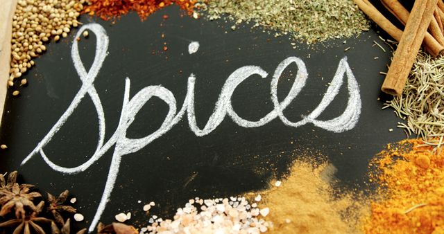 A variety of colorful spices are arrayed next to the word spices written in cursive on a chalkboard, with copy space. The assortment includes cinnamon sticks, star anise, and various ground spices, showcasing the diversity of flavors used in culinary arts.