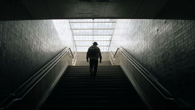 Lone Commuter Ascending Staircase Under Skylight in Symmetrical Urban Transit Passage