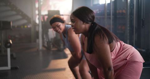 Two diverse women resting between reps, training together at gym and showing camaraderie