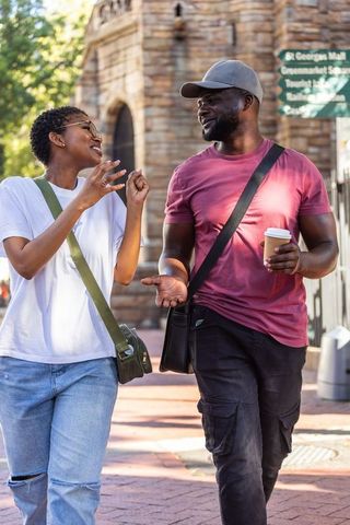 African american couple walking, talking and smiling in historic city holding coffee and bags