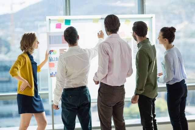 Business professionals collaborating on a project, brainstorming ideas on a whiteboard in a modern office. Ideal for illustrating teamwork, corporate meetings, strategic planning, and professional collaboration in business environments.