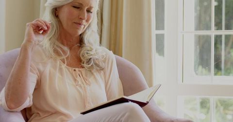 Senior Woman Writing Seated by Sunlit Window at Home