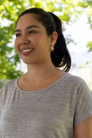 Sunlit woman smiling under trees in gray knit top with gold hoop earrings