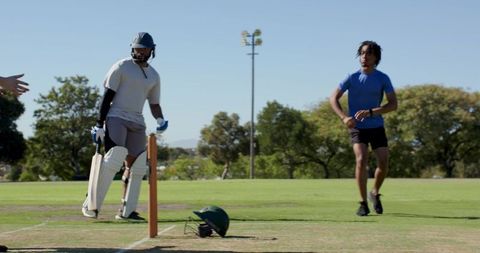 Indian batsman on cricket pitch holding bat with bowler running and helmet dropped