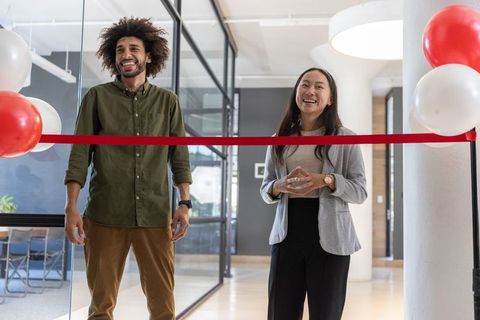 Diverse coworkers cutting ribbon in modern office inauguration ceremony