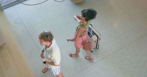 Couple walking through hotel lobby pulling rolling suitcase wearing summer clothes
