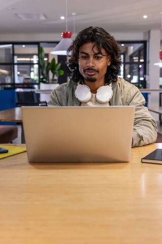 Indian young professional working on laptop in modern coworking space with headphones