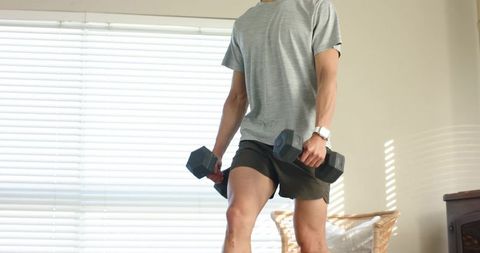 Asian man lifting dumbbells during home workout in sunlit living room