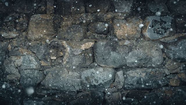 Weathered fieldstone wall under falling snow at night rustic masonry texture & lichen