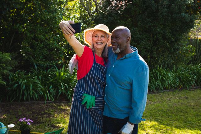Senior couple enjoying gardening together and taking a selfie, ideal for articles and campaigns about retirement lifestyle, family bonding, outdoor activities, and healthy aging.