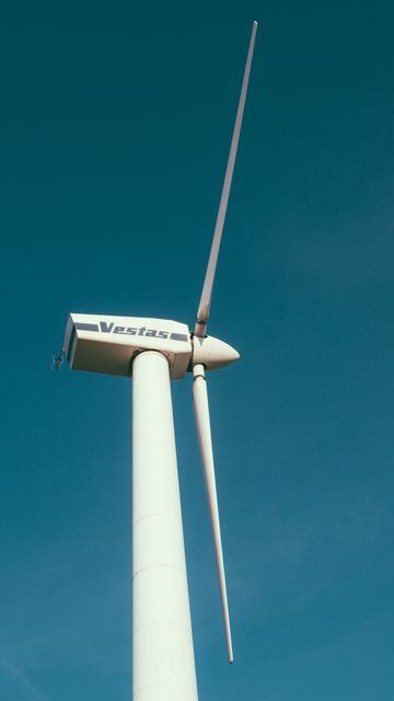 Image depicts a modern wind turbine set against a clear blue sky. The turbine, which is noticeably tall and sleek, is emblematic of renewable energy and sustainability efforts. This image can be used in contexts relating to green energy solutions, environmental conservation initiatives, or clean technology promotions. Ideal for websites, presentations, and marketing materials that focus on sustainable development and eco-friendly power sources.