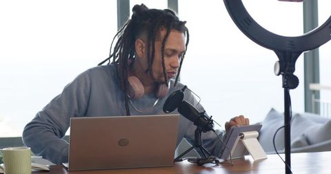 Podcasting and live streaming in sunlit home studio with laptop, microphone and ring light