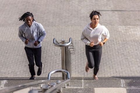 Running partners sprinting up urban steps wearing hoodies and smartwatches, outdoor fitness duo