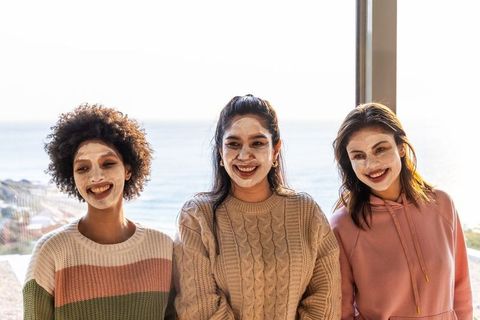 Multicultural friends wearing facial masks on sunny seaside balcony, smiling together