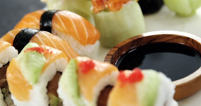 Assorted sushi pieces are elegantly presented next to a small bowl of soy sauce, with copy space. A variety of fresh toppings like salmon and avocado highlight the traditional Japanese cuisine's appeal.
