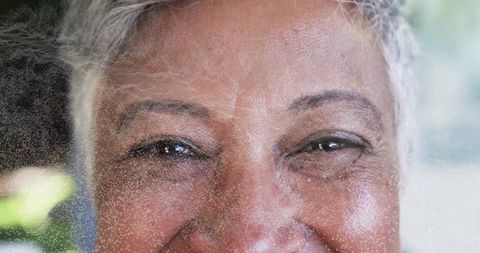 Gazing mature woman smiling through frosted film closeup showing gray hair and fine lines