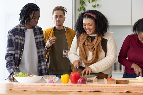 Diverse friends chopping vegetables together at kitchen island for cozy home cooking