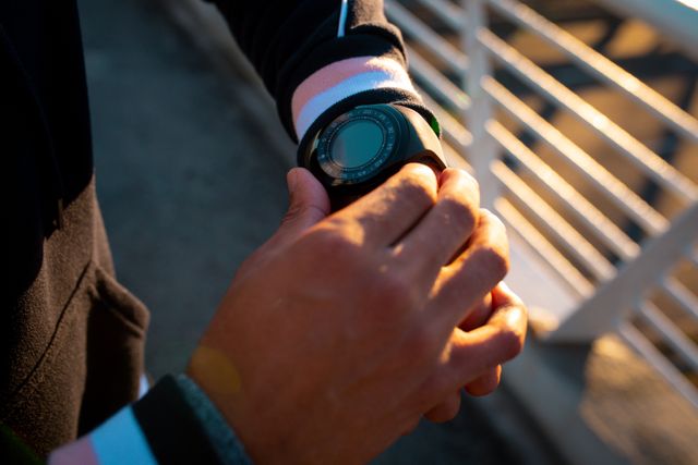 Hands of fit biracial man looking at smartwatch during training. healthy active lifestyle and outdoor fitness.