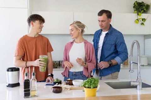 Family preparing green smoothie and chopping vegetables at bright modern kitchen island