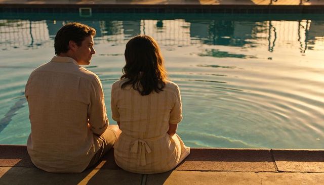 Couple sitting at pool edge wearing light linen, talking and gazing serene golden hour