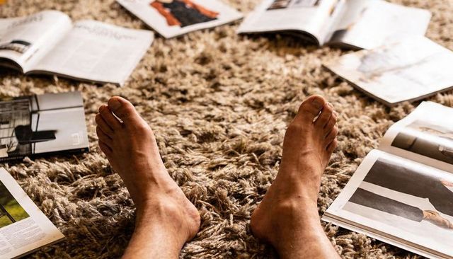 Bare feet resting on shag rug surrounded by open magazines
