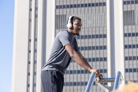 African american man leaning on railing listening with headphones against urban high-rise