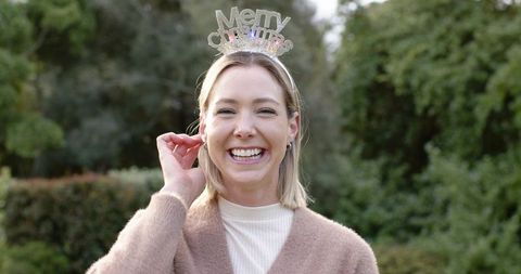 Mid-adult woman smiling and adjusting merry christmas tiara in garden holiday portrait