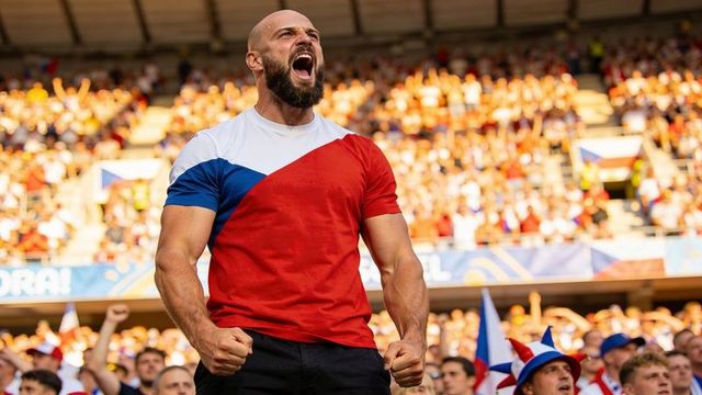Bearded fan cheering in red-white-blue shirt clenching fists in packed stadium crowd