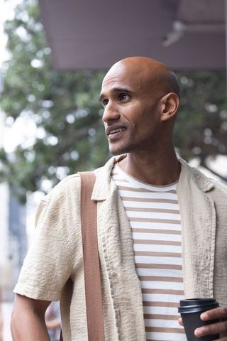 African american man holding coffee looking away on urban sidewalk in casual streetwear