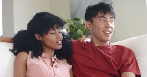 Multiracial couple relaxing on sofa at home enjoying cozy conversation