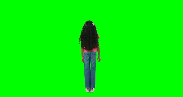 A young girl with curly hair stands facing away from the camera against a green screen background, with copy space. Her casual attire and the green screen suggest a setting that's ready for digital editing or special effects.