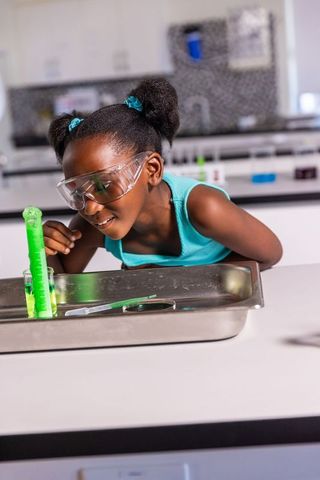 African american girl doing bubbling chemistry experiment in school lab wearing goggles