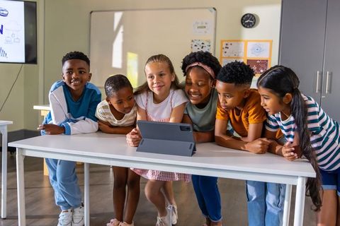 Elementary students leaning over tablet collaborating in multicultural classroom