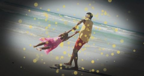 Spinning father swinging daughter on sunlit beach with playful bokeh and dark vignette
