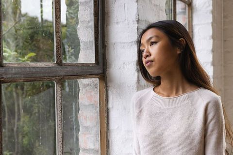 Young Woman by Window Reflecting on Rainy Day in Cozy Loft